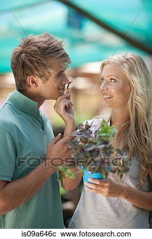 Stock Image - Couple smelling plant in nursery. Fotosearch