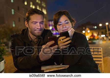 Stock Image - Couple using cell phones outdoors. Fotosearch