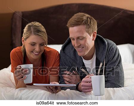 Stock Photograph - Couple using tablet computer on bed. Fotosearch