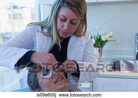 Stock Image - Doctor placing patches on patient's eyes. Fotosearch