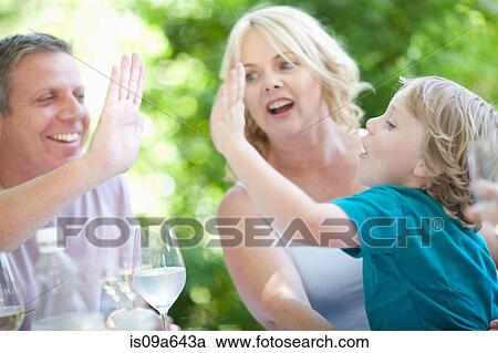 Stock Image - Father and son high fiving at table. Fotosearch