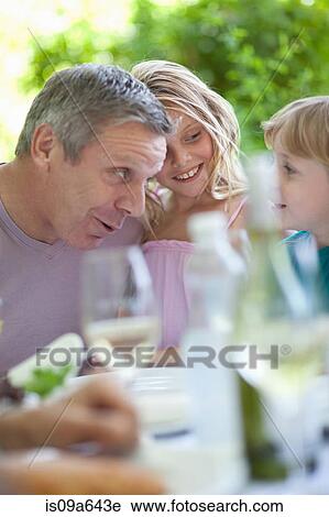 Stock Image - Father and son talking at table outdoors. Fotosearch