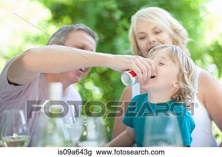 Stock Image - Father giving son soda at table. Fotosearch