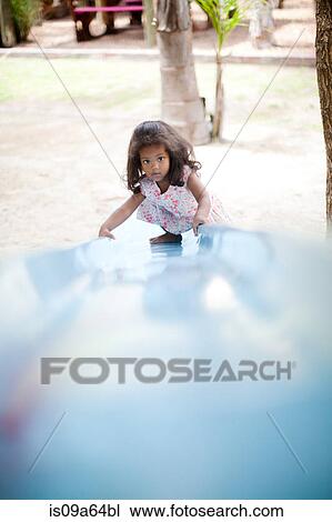 Stock Image - Girl climbing up slide at playground. Fotosearch