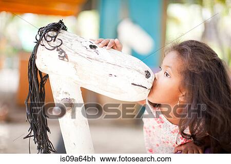 Stock Image - Girl kissing toy horse outdoors. Fotosearch