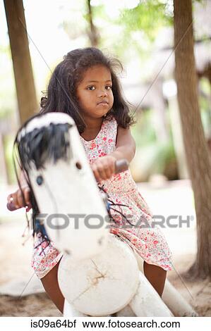 Stock Image - Girl playing on toy horse in park. Fotosearch