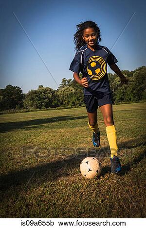 Stock Image - Girl playing soccer in field. Fotosearch