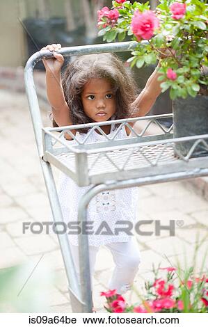 Stock Image - Girl pushing cart in plant nursery. Fotosearch