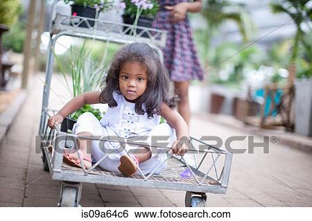 Girl sitting in cart at plant nursery View Large Photo Image Stock Photograph - Girl sitting in cart at plant nursery. Fotosearch