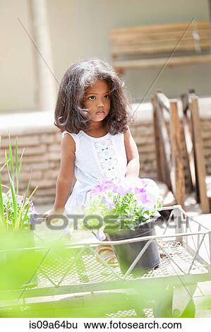Stock Photograph - Girl sitting on cart in flower nursery. Fotosearch