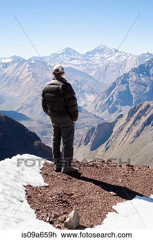 Stock Image - Hiker overlooking snowy mountains. Fotosearch
