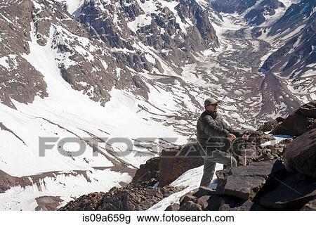 Stock Image - Hiker walking on rocky mountainside. Fotosearch