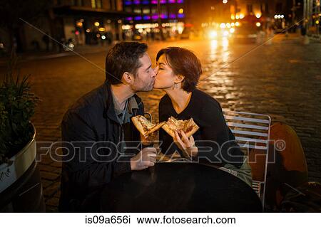 Stock Image - Kissing couple having pizza outdoors. Fotosearch