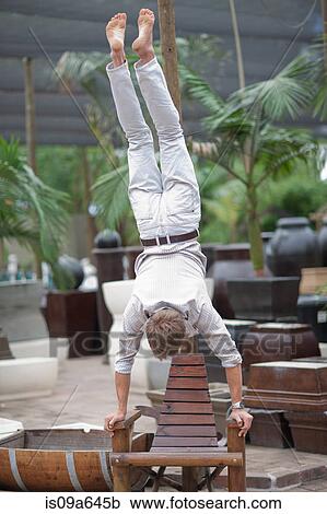 Stock Image - Man doing handstand on lawn chair. Fotosearch