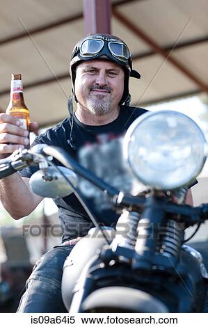 Stock Photography - Man drinking beer on motorcycle. Fotosearch