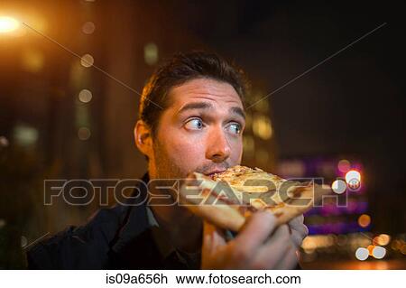 Stock Image - Man eating pizza on city street. Fotosearch