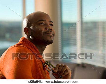 Stock Photograph - Man holding eyeglasses in living room. Fotosearch
