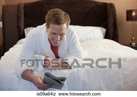 Stock Photo - Man reading newspaper on bed. Fotosearch
