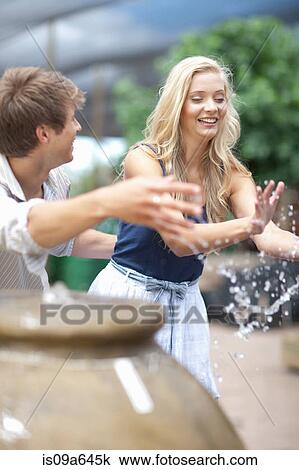 Stock Image - Man splashing girlfriend in fountain. Fotosearch