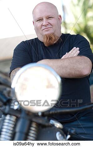 Stock Photo - Man standing by motorcycle. Fotosearch