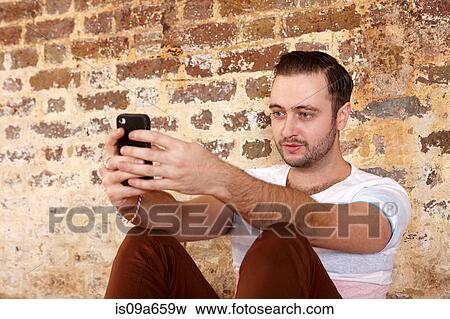 Man using cell phone by brick wall View Large Photo Image Stock Photo - Man using cell phone by brick wall. Fotosearch