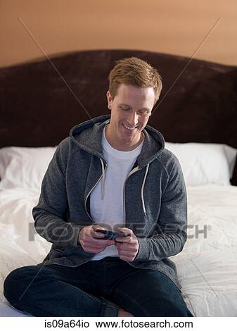 Picture - Man using cell phone on bed. Fotosearch