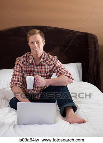 Stock Photo - Man using laptop on bed. Fotosearch