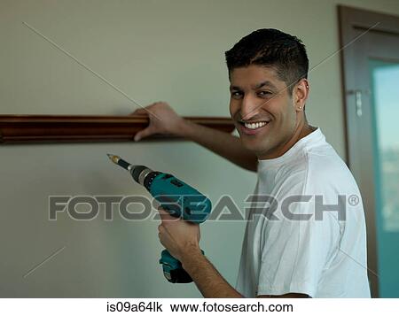 Stock Image - Man using power drill in living room. Fotosearch