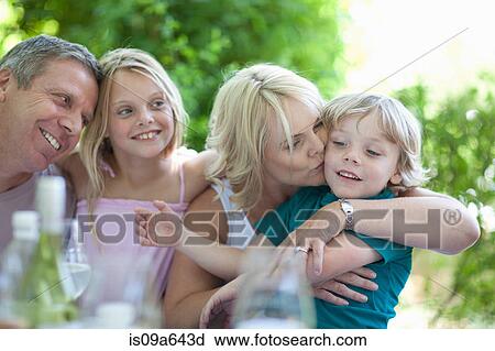 Stock Image - Mother kissing son at table outdoors. Fotosearch