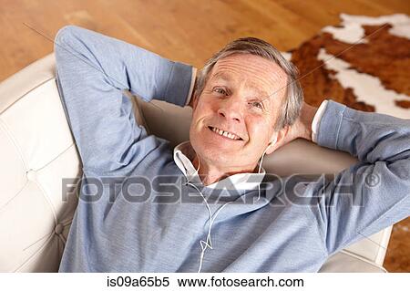 Stock Photography - Older man listening to earphones on sofa. Fotosearch