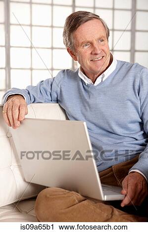 Stock Image - Older man using laptop on sofa. Fotosearch