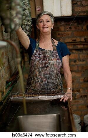 Picture - Older woman standing at sink. Fotosearch