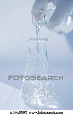 Stock Image - Scientist pouring liquid into beaker. Fotosearch