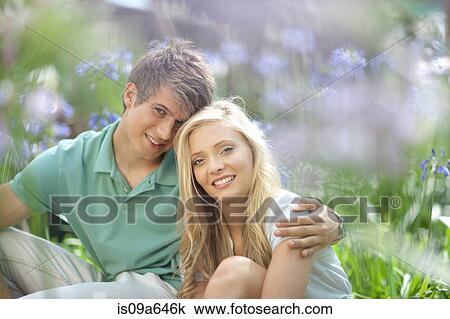 Stock Image - Smiling couple sitting in tall plants. Fotosearch