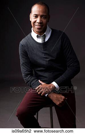Stock Image - Smiling man sitting on stool. Fotosearch
