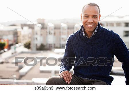 Stock Image - Smiling man sitting on urban balcony. Fotosearch