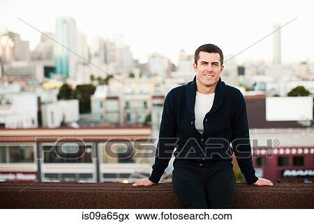 Stock Photo - Smiling man sitting on urban balcony. Fotosearch