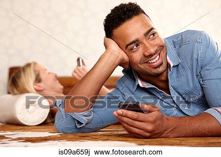 Stock Image - Smiling man using cell phone indoors. Fotosearch