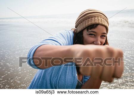 Stock Image - Smiling woman making fists on beach. Fotosearch