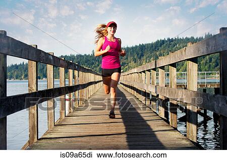 Stock Image - Teenage girl running on wooden dock. Fotosearch