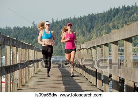 Stock Photo - Teenage girls running on wooden dock. Fotosearch