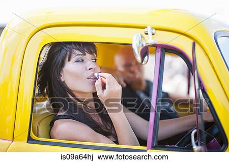 Stock Image - Woman fixing makeup in car mirror. Fotosearch