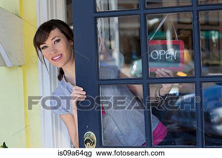 Stock Image - Woman hanging open sign in door. Fotosearch