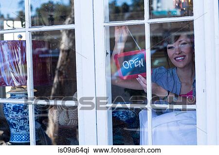 Stock Image - Woman hanging open sign in door. Fotosearch