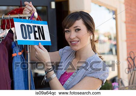 Stock Image - Woman hanging open sign on clothes rack. Fotosearch