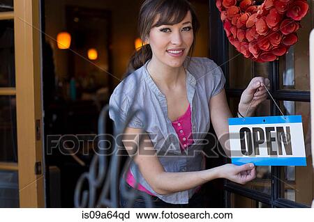 Stock Image - Woman hanging open sign on door. Fotosearch