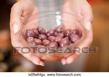 Stock Photograph - Woman holding bowl of olives in grocery. Fotosearch