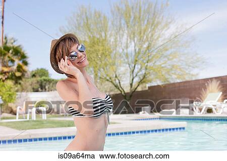 Stock Image - Woman in bikini standing by pool. Fotosearch