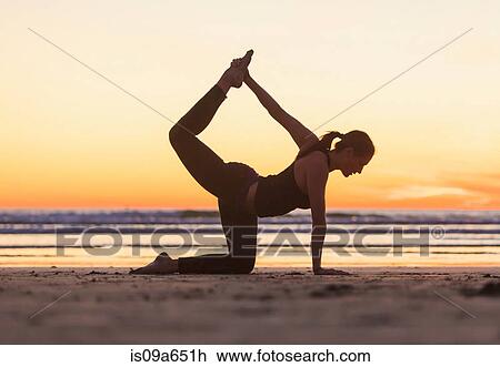 Stock Image - Woman practicing yoga on beach. Fotosearch