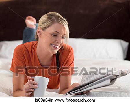 Stock Photography - Woman reading newspaper on bed. Fotosearch